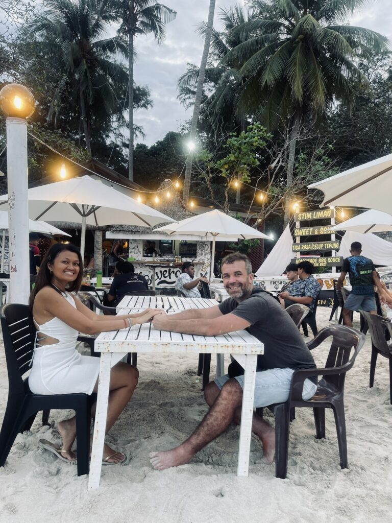 "Roman and Fizah enjoying a beachfront lunch at Perhentian Island with a stunning ocean view."